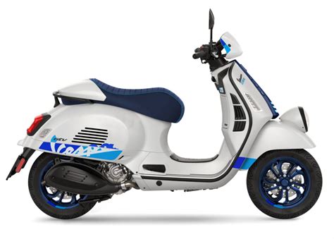 Gros plan sur les détails de la Vespa 140th : phare bas, guidon tubulaire, selle bleue et jantes spécifiques.