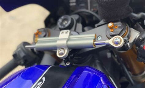 Schéma d'un amortisseur de direction monté sur une moto, montrant les points de fixation et le vérin.