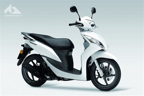 Vue latérale d'un scooter Honda Vision 50 gris, stationné dans une rue urbaine animée.