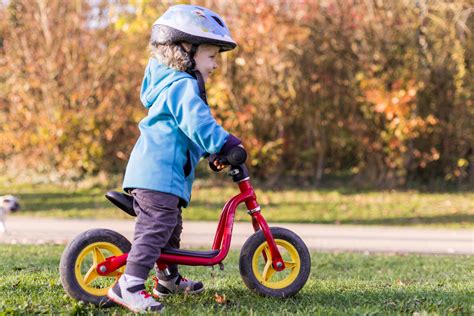 Enfant souriant en train de faire de la draisienne en bois dans un parc