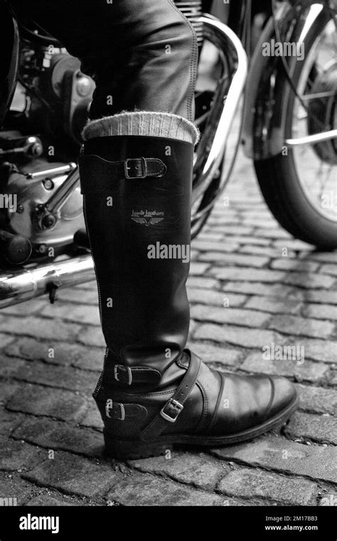 Image d'un motard portant des bottes en cuir marron robustes, sur une moto customisée.
