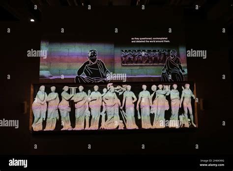 Une illustration représentant des penseurs grecs débattant, avec des figures d'esclaves en arrière-plan.