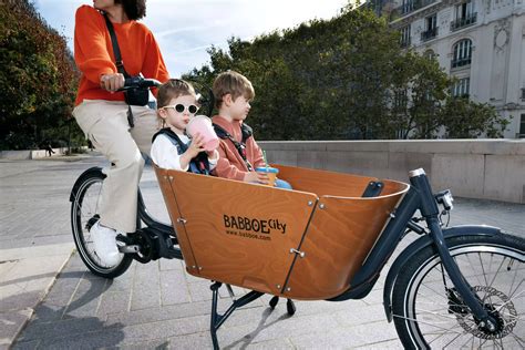 Une famille souriante installée dans un vélo cargo Christiania Bikes Familial, avec des sacs de courses.