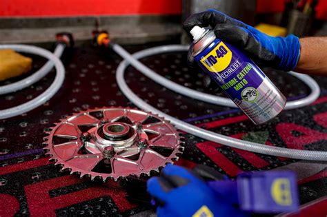 Image montrant l'application d'un nettoyant sur une chaîne de moto et l'utilisation d'une brosse